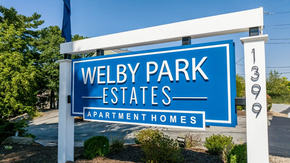 A welcoming sign amidst a backdrop of lush greenery reads 'Welby Park Estates Apartment Homes'.