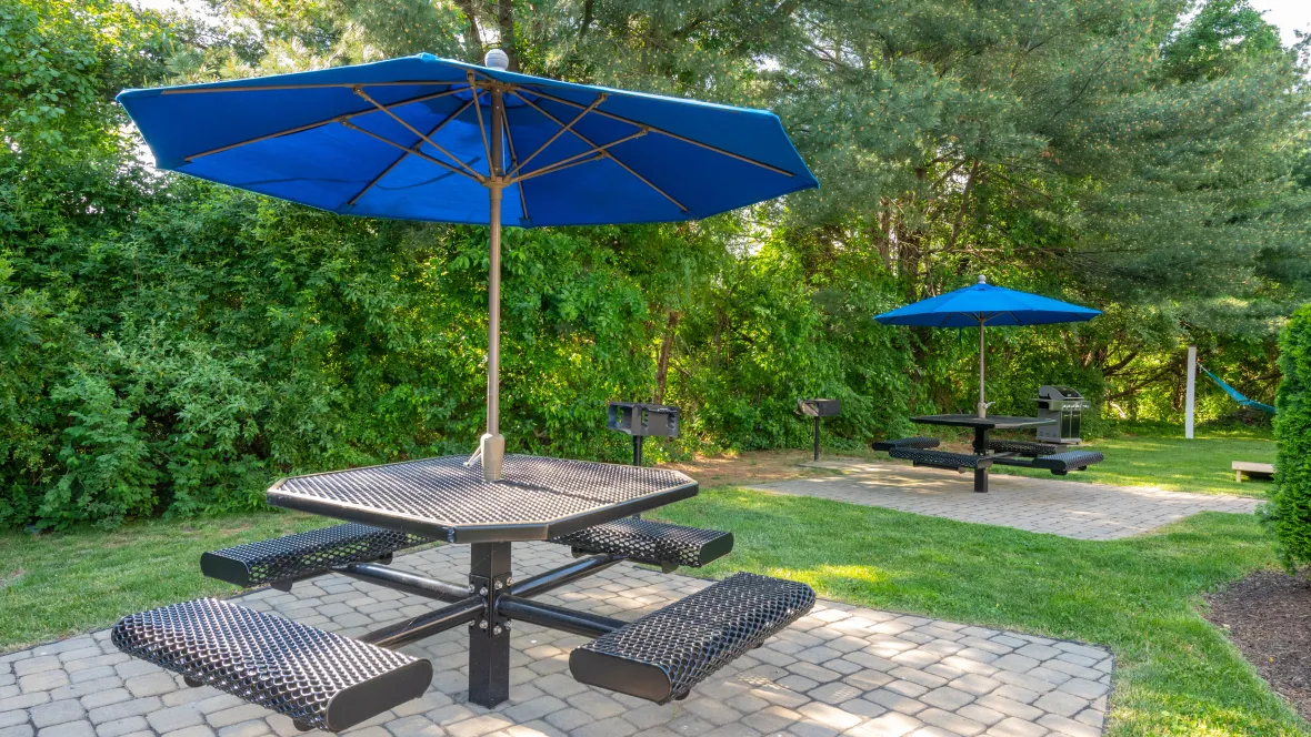 Two umbrella-covered picnic tables on paved pads with grilling options accessible for residents.