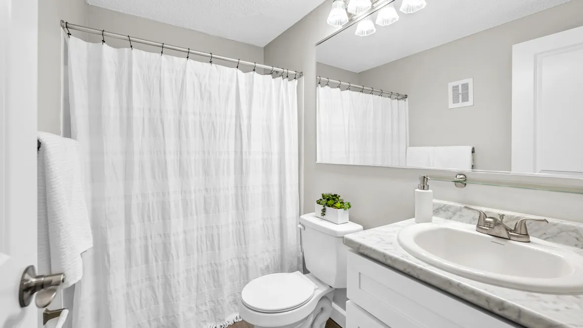 A well-lit bathroom with superior elements, including an expansive mirror and gleaming cabinetry.