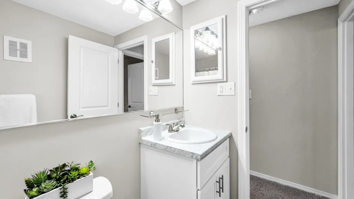 A bright bathroom with a generously sized mirror, pristine white cabinetry, and gleaming marble-style countertops that convey a sense of refinement.