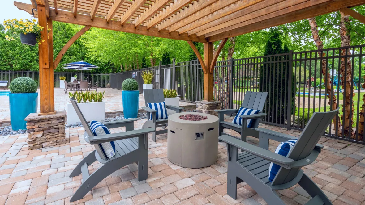 A tranquil fireside oasis with a firepit and Adirondack seating under an elegant pergola.