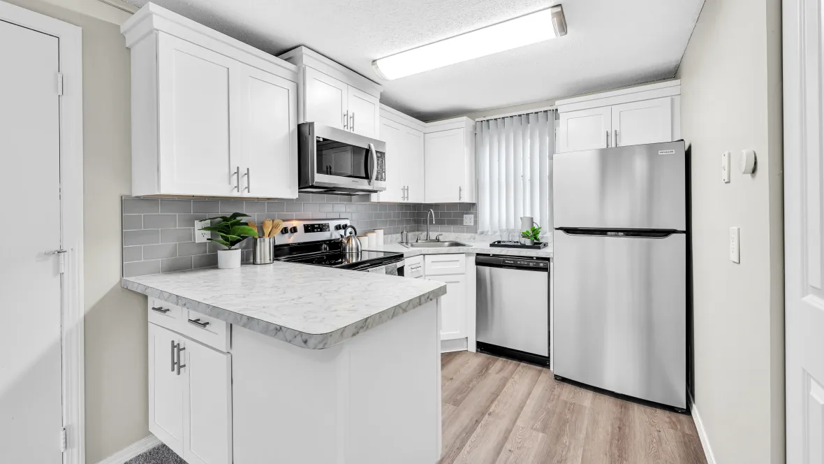 An elegant, well-lit kitchen with timeless white cabinetry, white Carrara-inspired countertops, gleaming appliances, and a chic tile backsplash. .