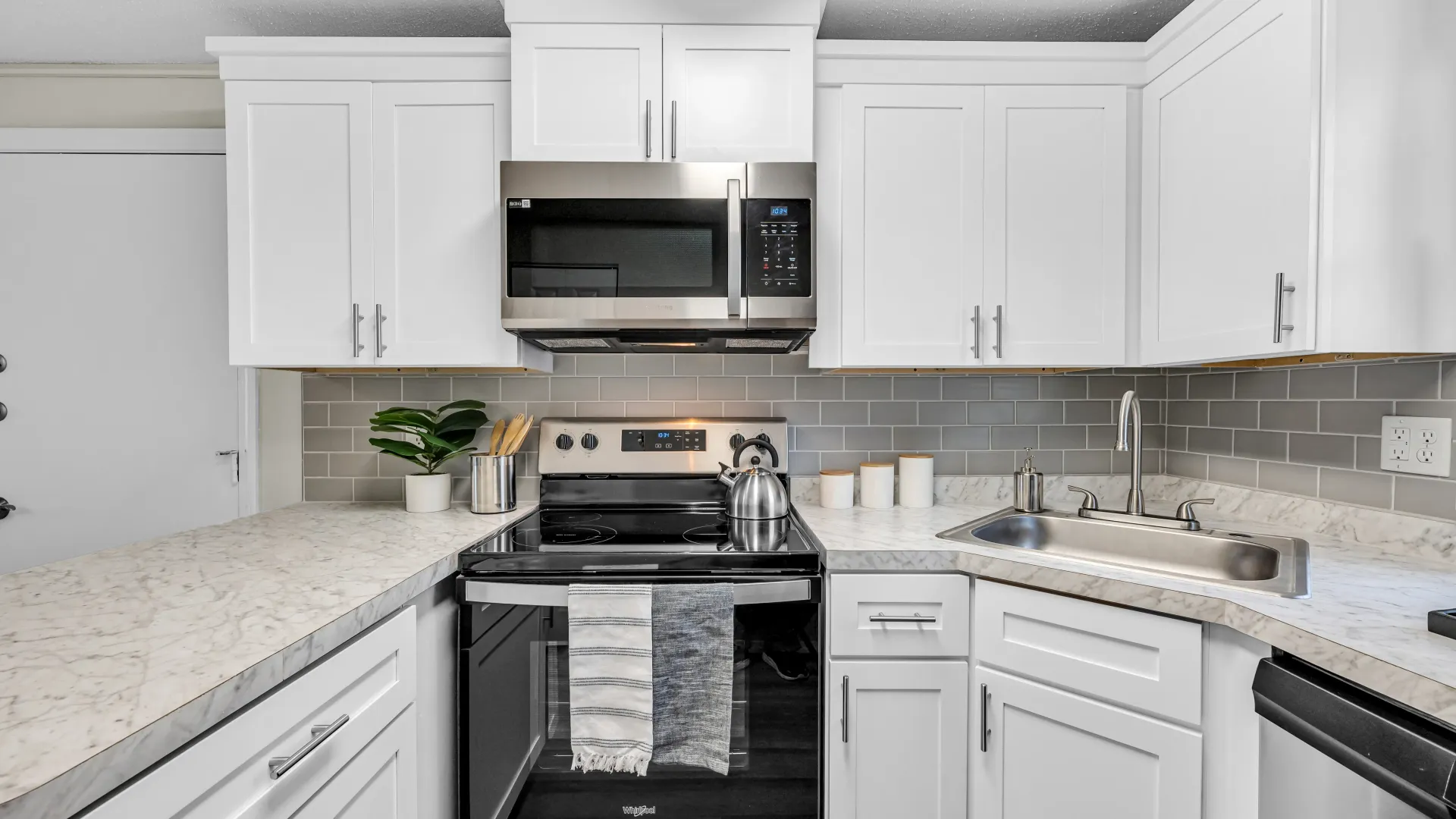 Kitchen outfitted with sleek stainless-steel appliances with a look at the stove and microwave with a slick grey backsplash. 