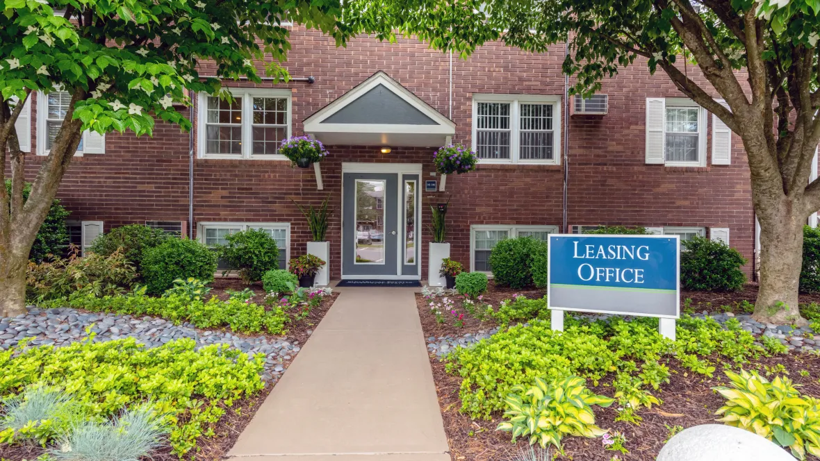 Exterior of the leasing office with welcoming signage reading “Leasing Office” and lush landscaping on either side of the walk path to the entry.