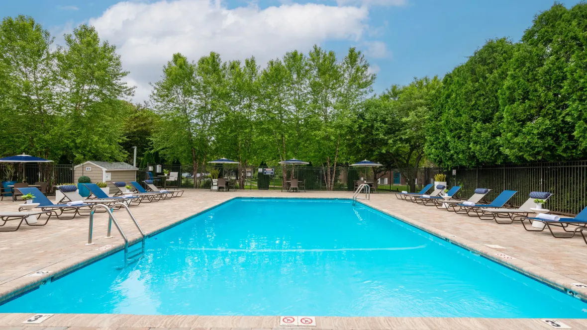 A glistening pool surrounded by a spacious pool deck with chic loungers, offering ample room for leisure for all. 