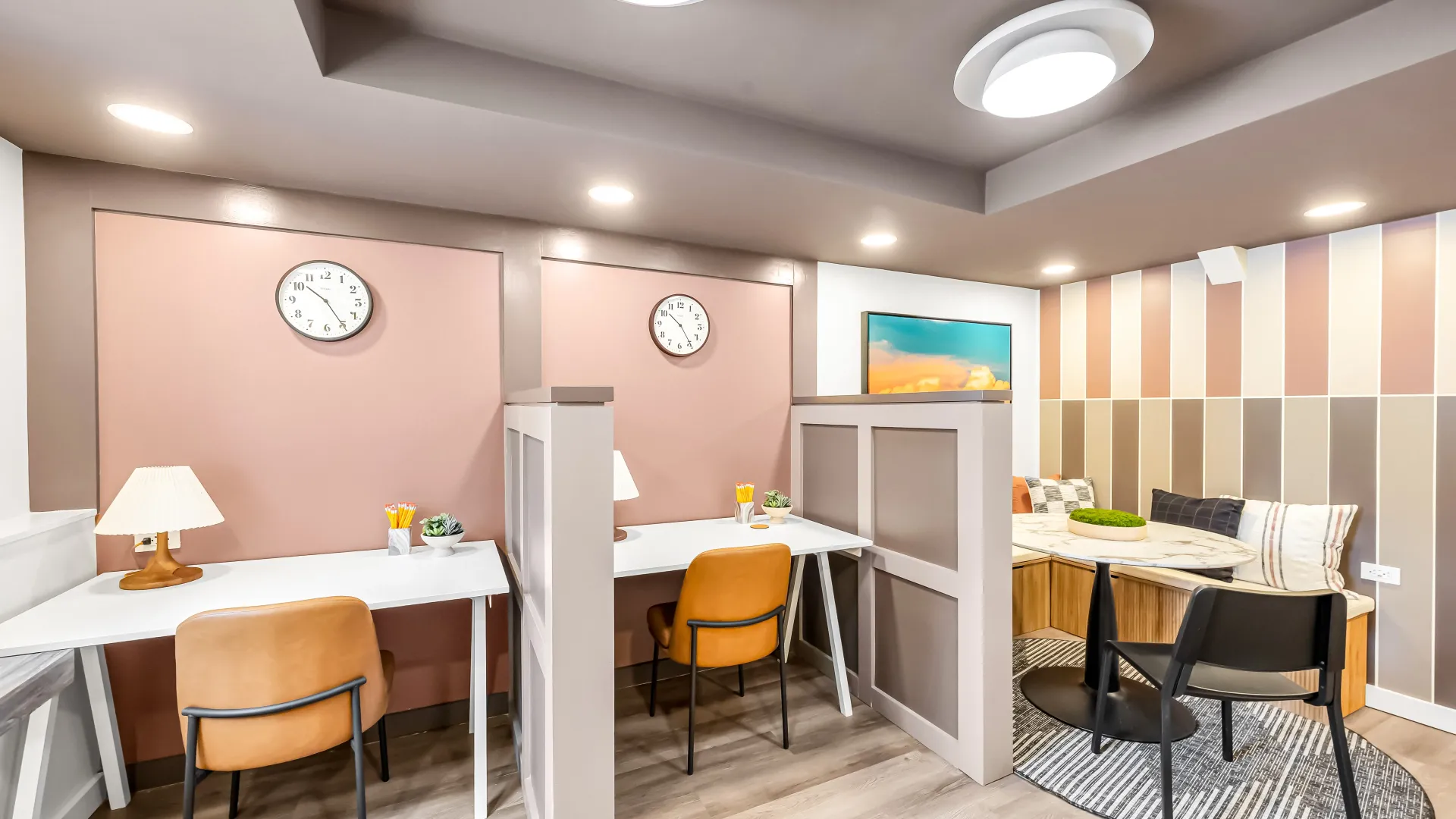 Two desks with orange chairs and desks separated by partitions with a table and chairs on the side.