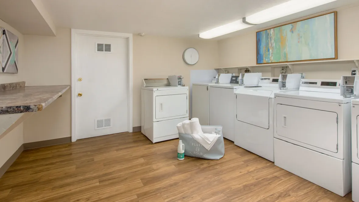 View of the community laundry room's interior, featuring bright lighting and multiple washer and dryer sets for residents' convenience.