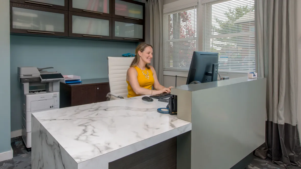 A welcoming leasing office with a friendly staff member sitting at the leasing desk - smiling and ready to assist!
