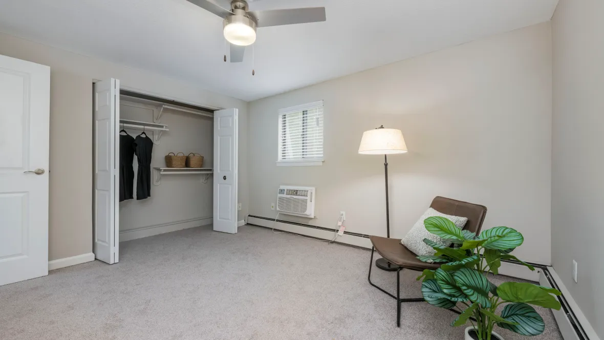 A large bedroom offering a roomy closet with shelves for essentials, a modern ceiling fan, and an air conditioner unit for added comfort.