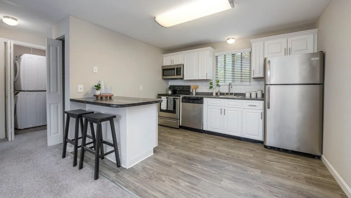 An elegant, inviting kitchen with wood-style flooring, black fusion granite-style countertops, white cabinetry, and stainless steel appliances.