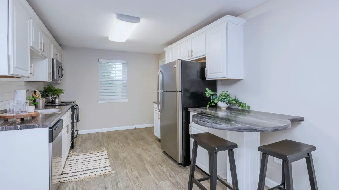 Charming galley-style kitchen with modern white cabinetry, stainless steel appliances, wood-like flooring, and a cozy breakfast bar for morning delights.