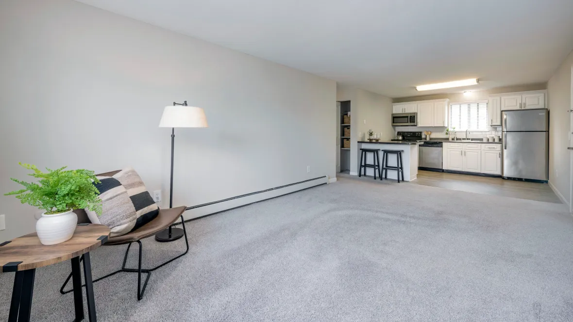 Expansive, open living room with cozy carpet and baseboard floor heaters, leading to the open kitchen.