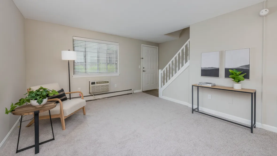 Spacious living room with cozy carpeting, large window, and a staircase with a white banister leading upstairs.