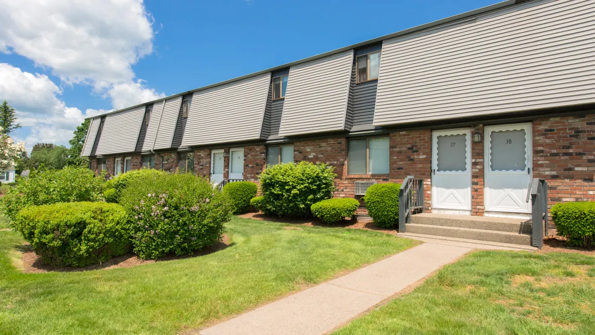 A classy red brick building with manicured green lawn and shrubbery, creating a welcoming path to your home.