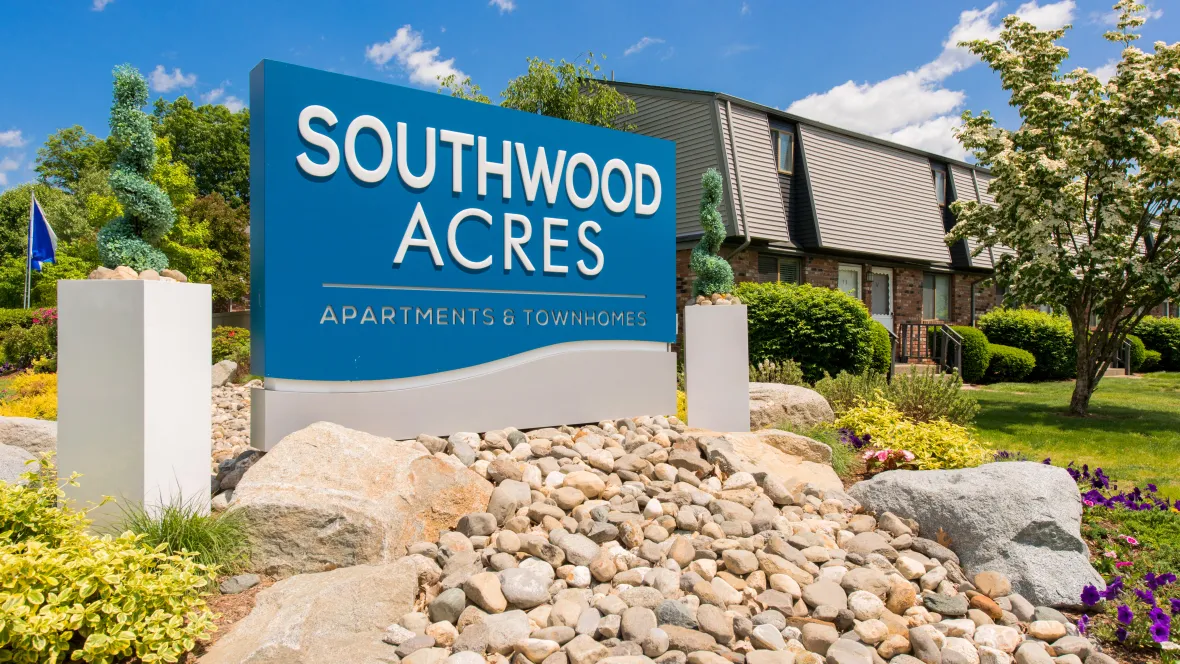 Entrance sign 'Southwood Acres Apartments & Townhomes' surrounded by lush, cascading rocks and greenery, creating a vibrant welcome.