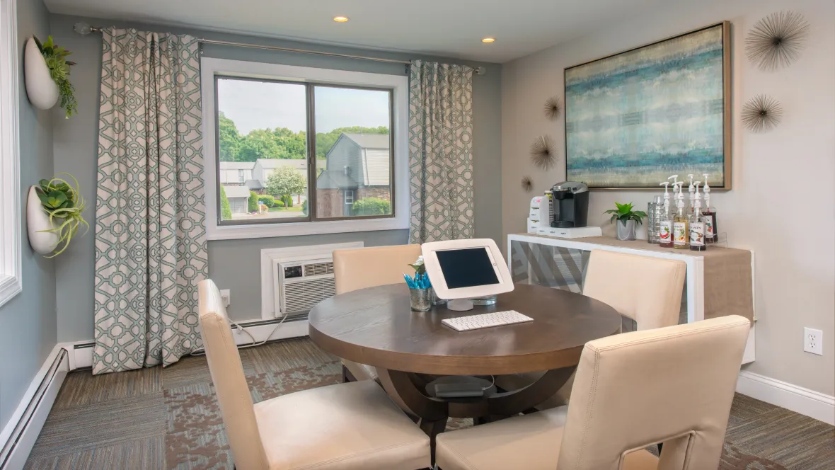 A picturesque leasing office interior with an open window, a table, and comfortable chairs for prospects to interact with property management experts.