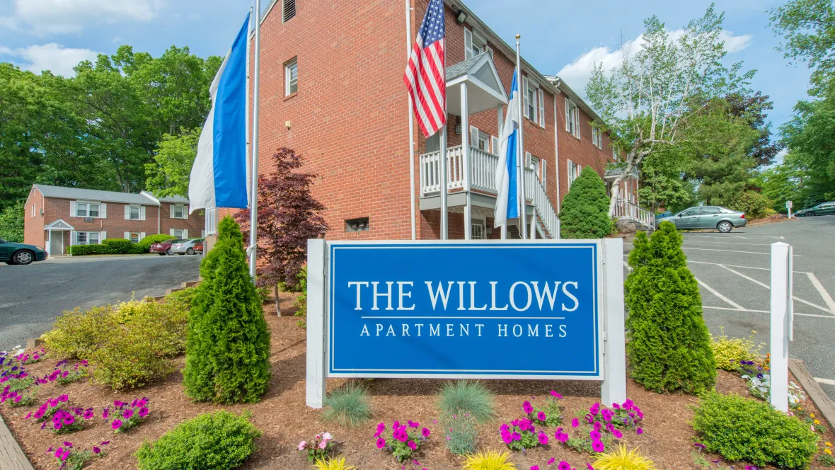 The front sign at the community entrance that reads “The Willows Apartment Homes,” surrounded by vibrant landscaping.