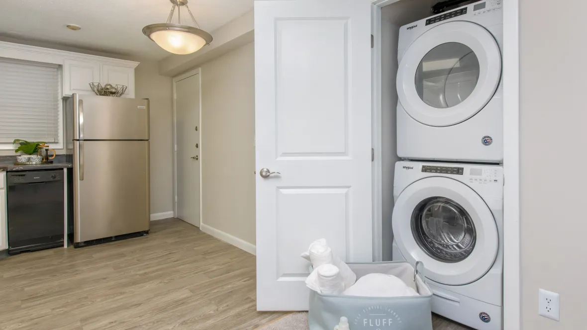 A complete laundry setup with stackable, full-size washer and dryer discreetly positioned in closet off the kitchen and living room for ultimate convenience.