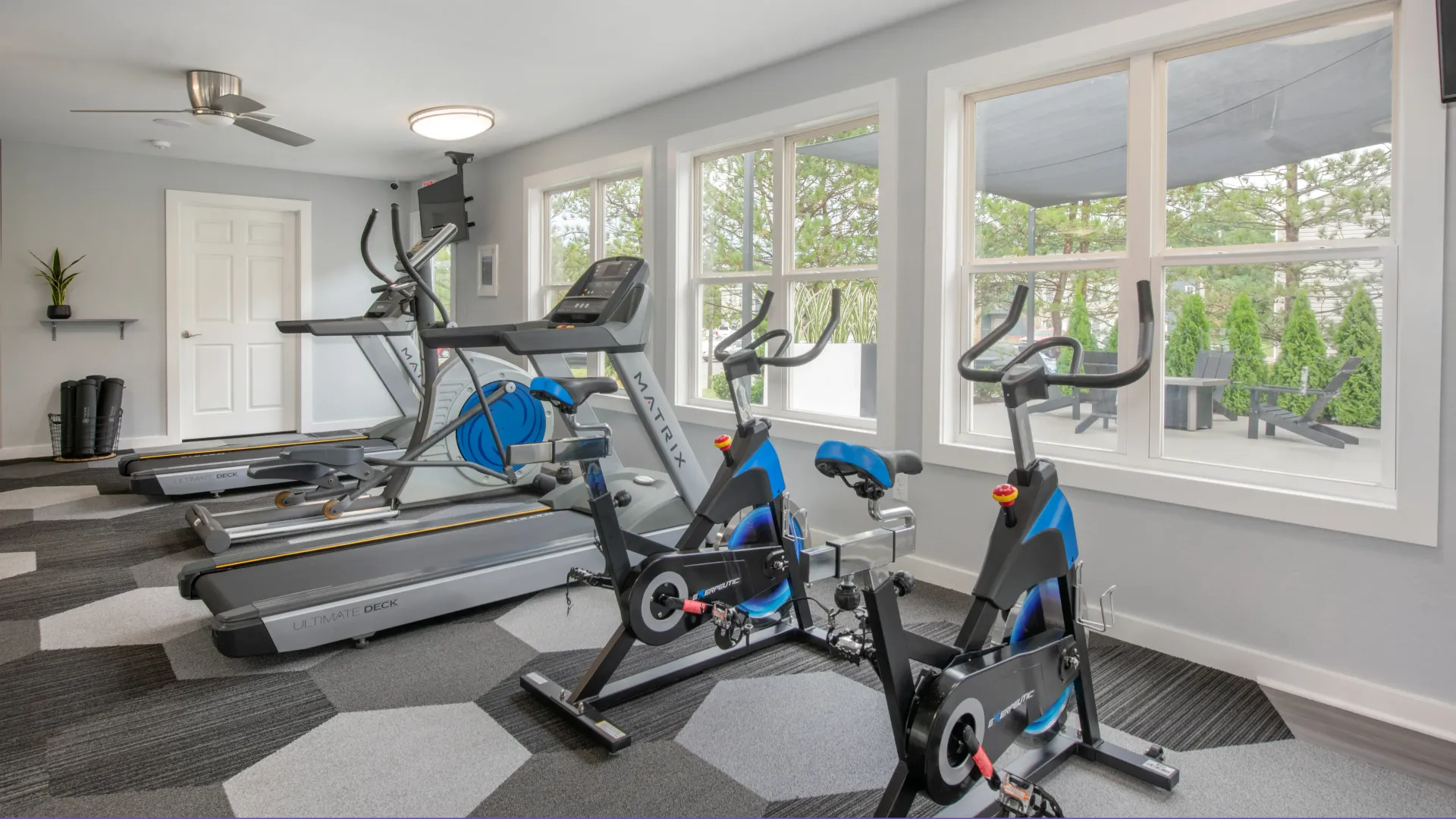 A variety of cardio equipment with a view of the outdoor patio and firepit, a glimpse of relaxation after your workout.