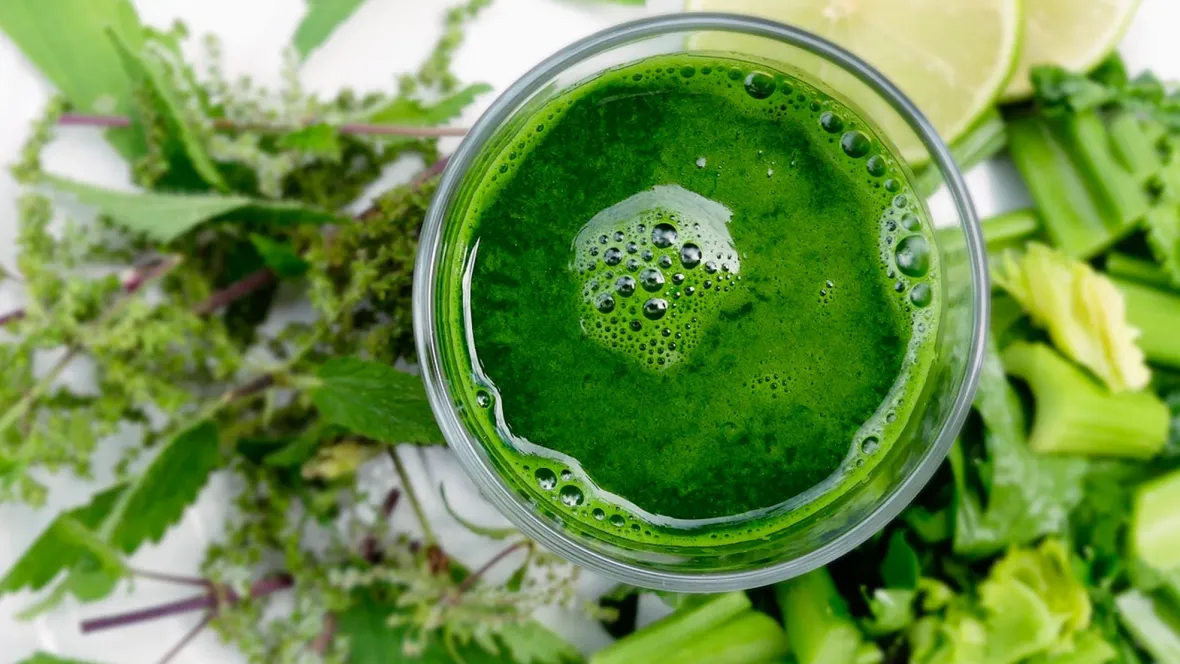 A green smoothie surrounded by fruits and veggies