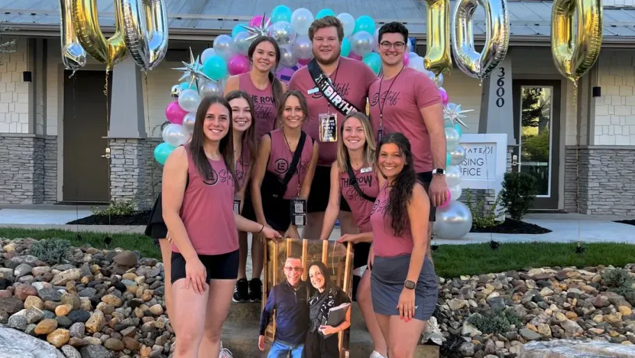 The Elevate 231 team gathered for a team photo in front of a colorful balloon arc with balloons on either side reading "100".