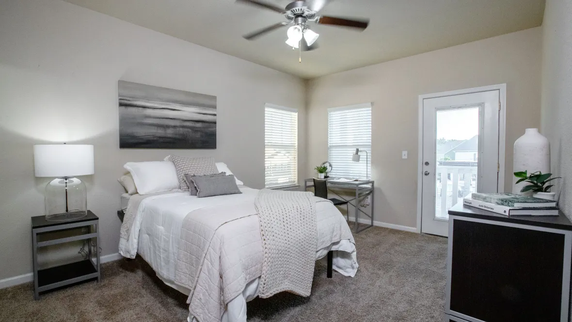 A spacious bedroom with two windows and a glass door for ample natural lighting and private balcony access.