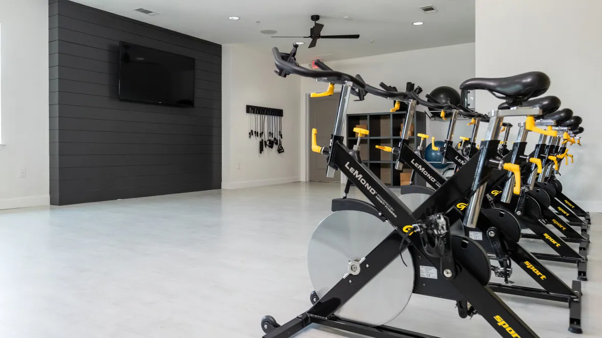 An aerobic studio attached to the fitness center, featuring spin bikes facing a mounted television.