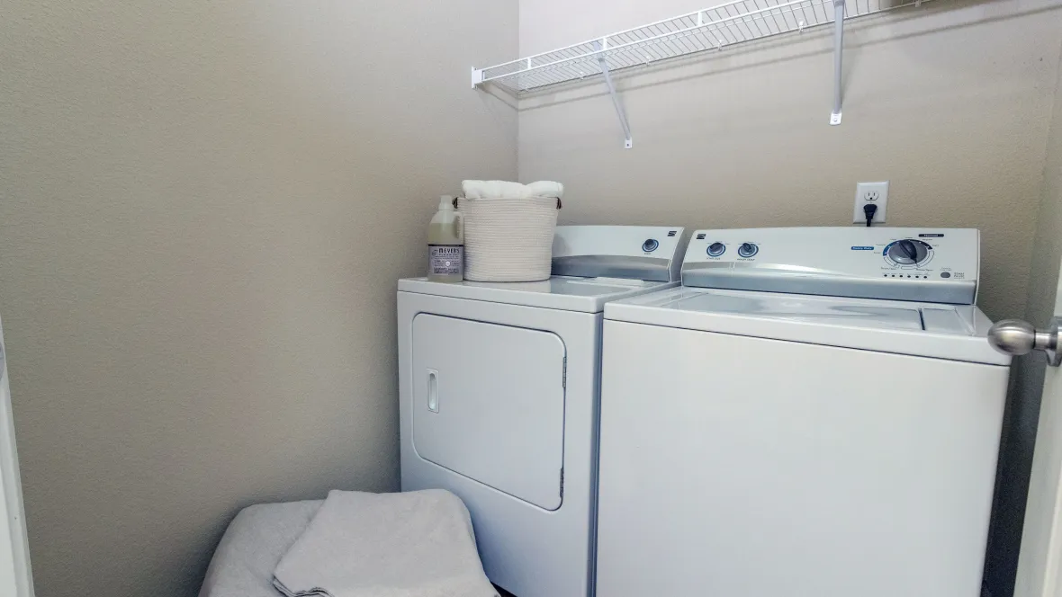 A laundry room with a full-size, side-by-side washer and dryer with mounted shelf above the appliances.