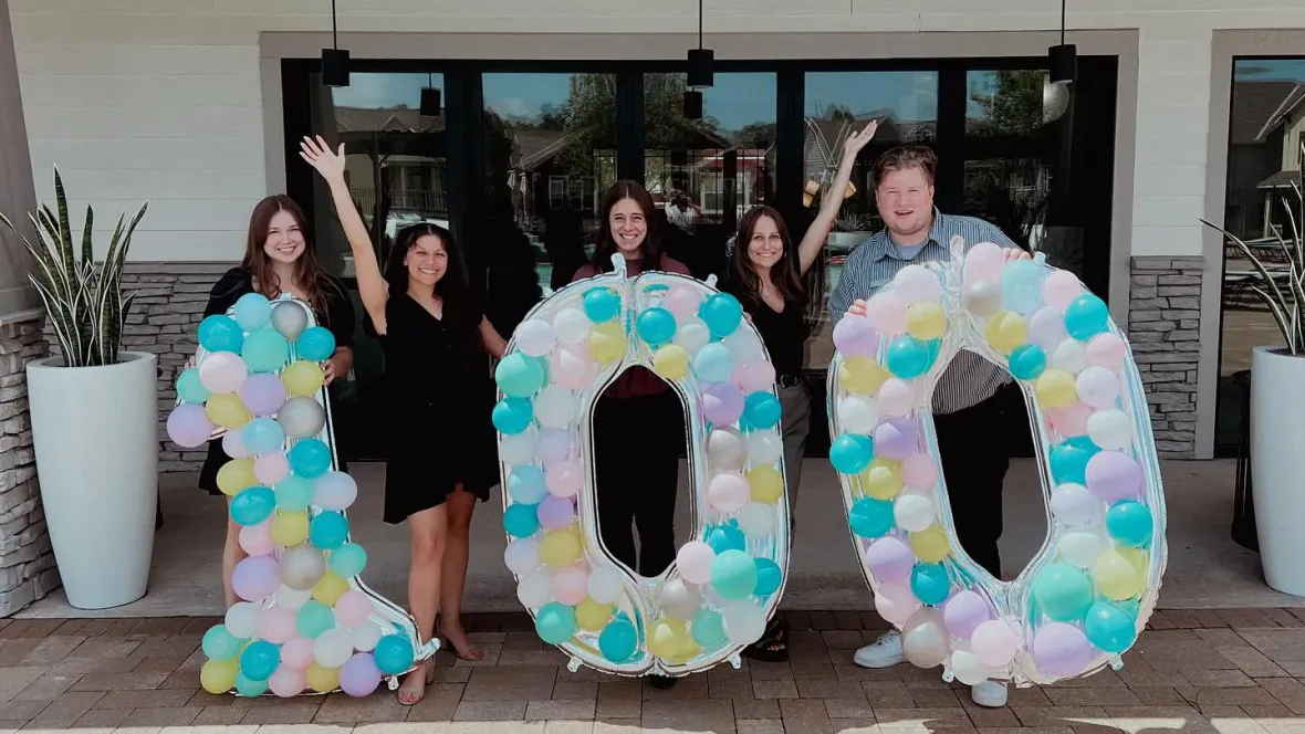 The Elevate 231 team gathered for a photo behind a large "100" covered in colorful baloons.