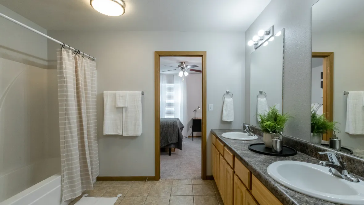 A roomy shared bathroom with a shower/tub combo, multiple mirrors, generous countertop space between double sinks, and ample storage space under the counter.