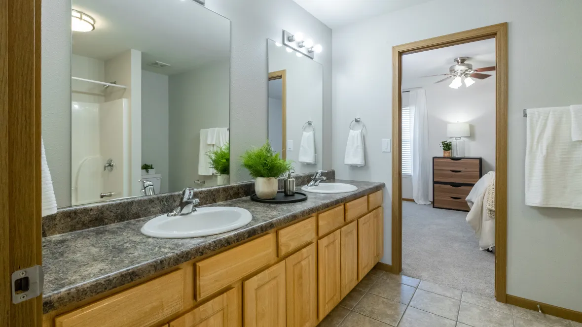 A well-lit bathroom complete with double sinks, large double mirrors, ample undersink cabinetry, and spacious countertops.
