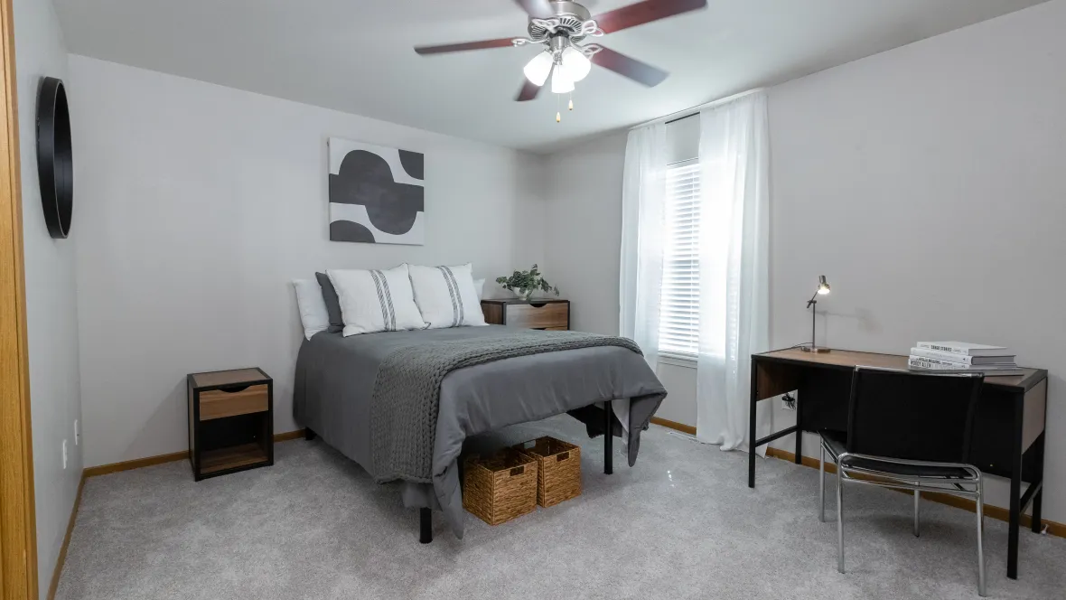 A brilliantly lit, fully-furnished student bedroom with plush carpeting and a ceiling fan with lights designed to get the most out of off-campus living.