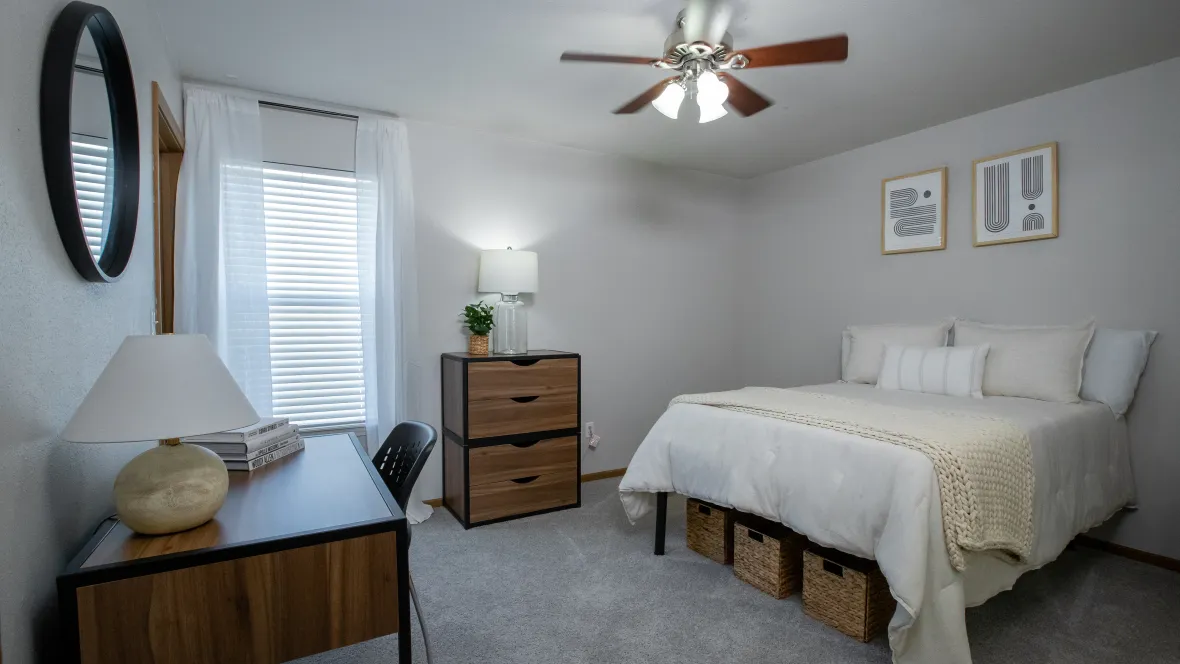 A completely furnished bedroom equipped for college life, featuring a full-size bed, dresser, nightstand, and desk.