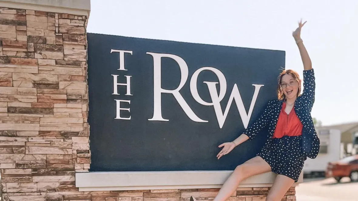 An employee sitting on The Row sign with their arms out showcasing the signage.