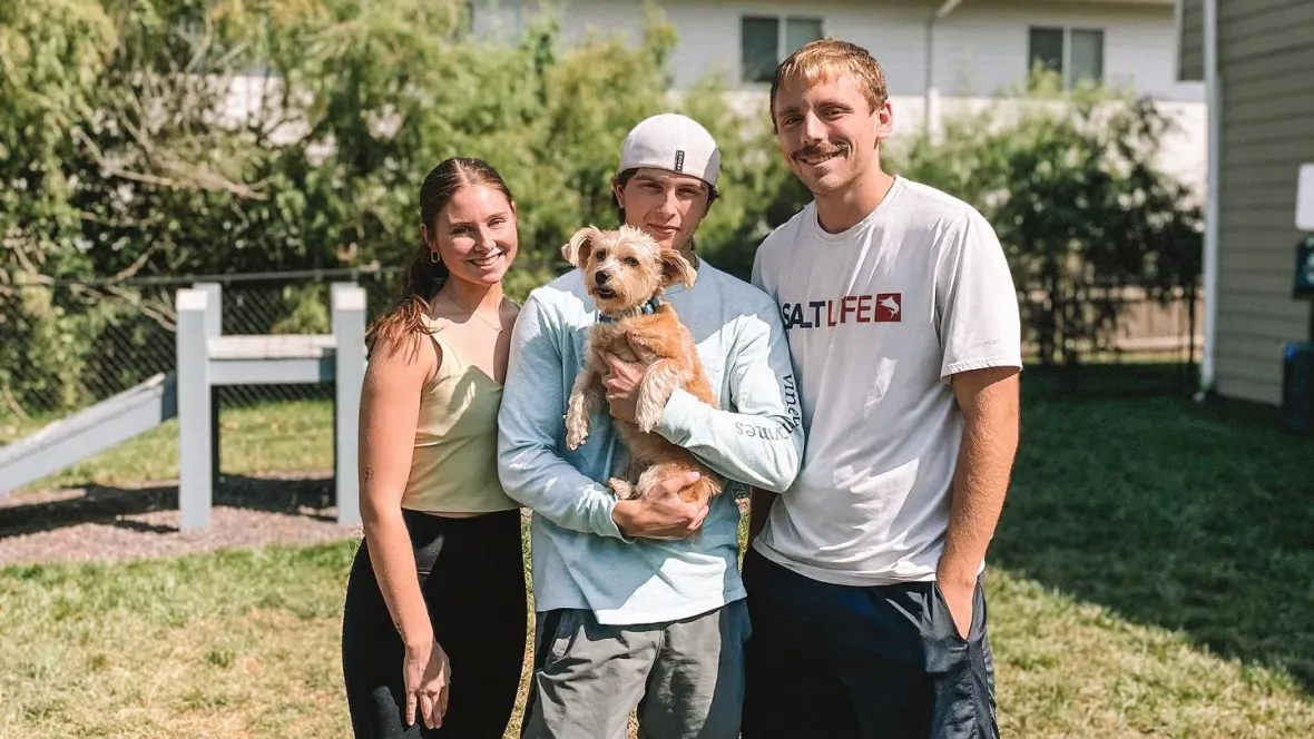 Three residents gather for a photo holding a small dog.