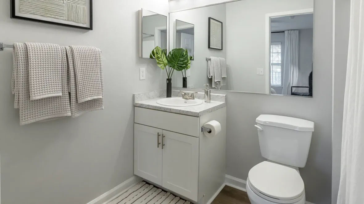 Brightly lit bathroom with an extensively wide mirror located above the sink and toilet. 