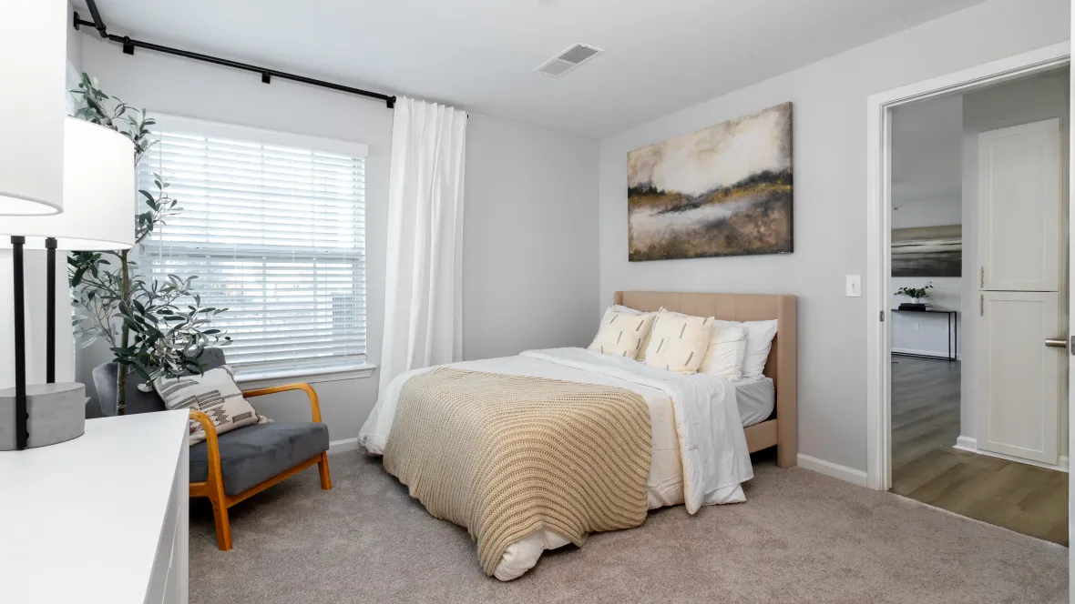 A spacious bedroom with plush carpeting highlighted by two wide windows offering abundant sunlight controlled with adjustable wood-style blinds. 