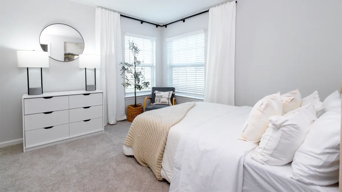 A large bedroom adorned with soft carpeting and two large windows that meet at one corning, offering an inviting atmosphere with optimal natural light.