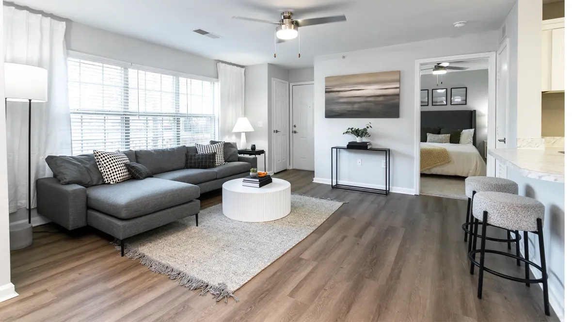 A stylish living area featuring wood-reminiscent flooring extending seamlessly from the entryway to the expansive living space, offering a preview of the plush carpeting in the master bedroom.
