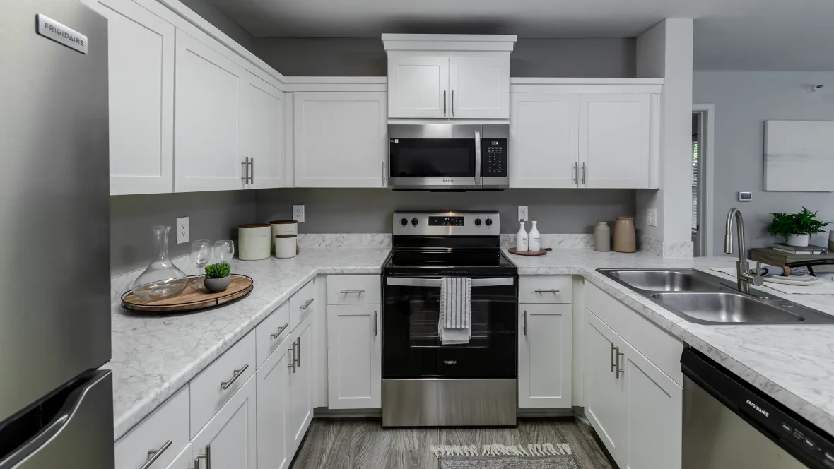 A u-shaped kitchen offering plentiful counterspace that opens to the living room and features stainless steel appliances, a microwave over the stove, and a large double sink. 