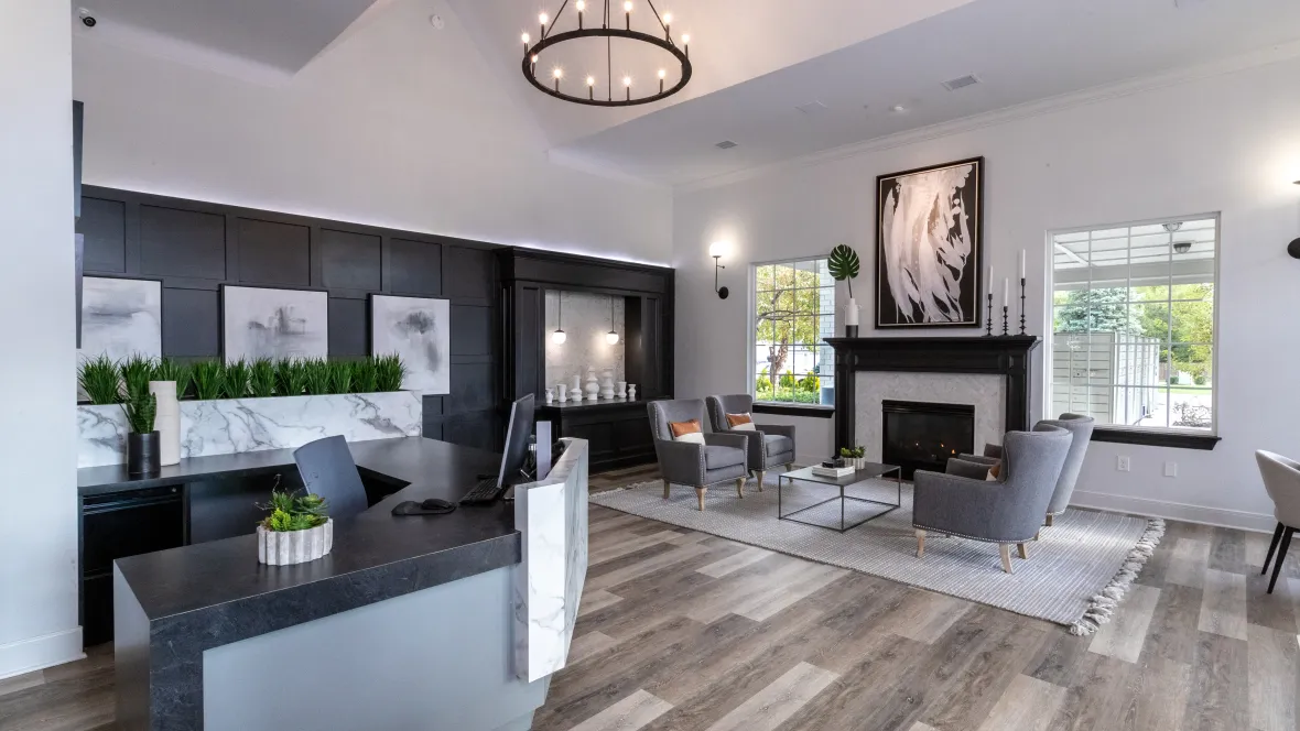 A stylish and modern leasing center interior with a neutral color palette and elegant decorations including a black-ringed chandelier, a black accent wall, and white and black decorations throughout.
