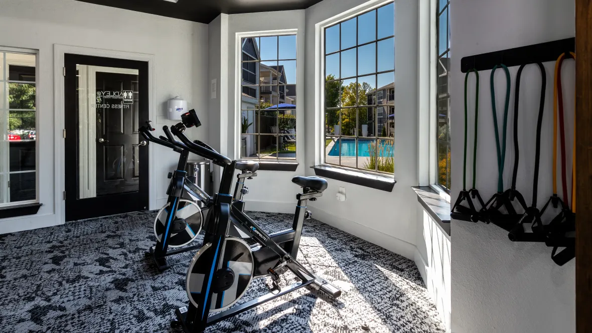 Two spinning bikes in our fitness center with windows behind where you can see the sparkling blue pool.