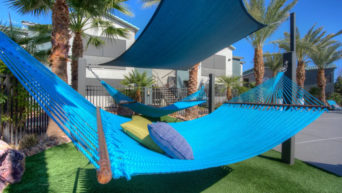 A serene hammock garden of two blue loungers swaying in a corner of the pool deck equipped with luxurious faux green grass underfoot for a truly luxe feel.  