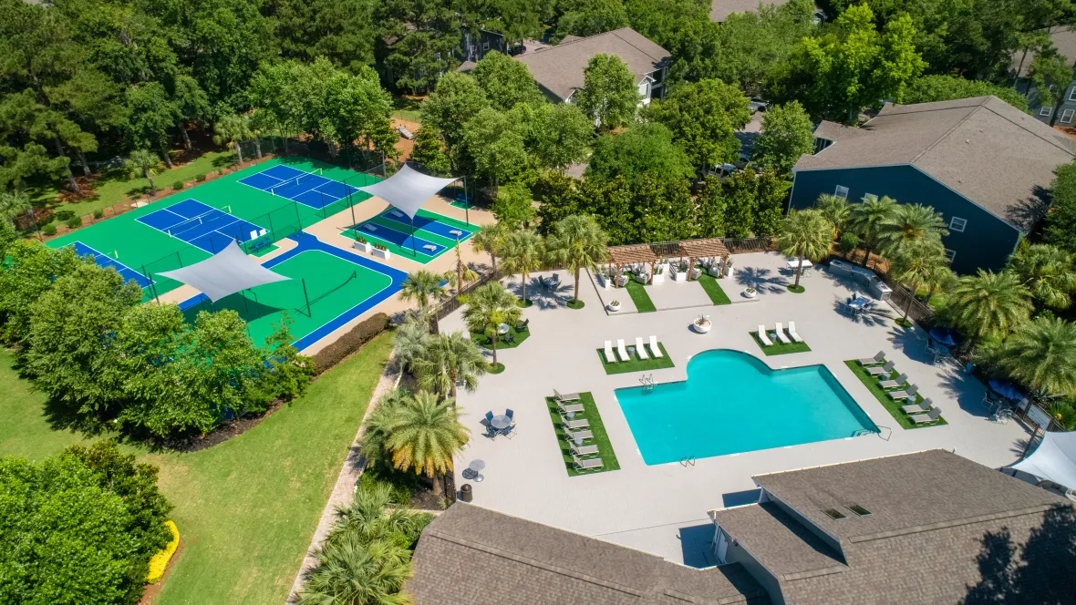 A breathtaking aerial view of Emerson Isles highlighting apartment rooftops, sports courts, and the vibrant pool deck with a poolside kitchen, loungers, and fire pit.