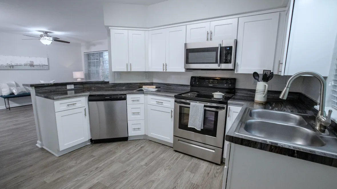 A spacious kitchen with black fusion countertops, white shaker cabinetry, and stainless-steel appliances. This angle showcases the stove, microwave, dishwasher, and abundant cabinet space.