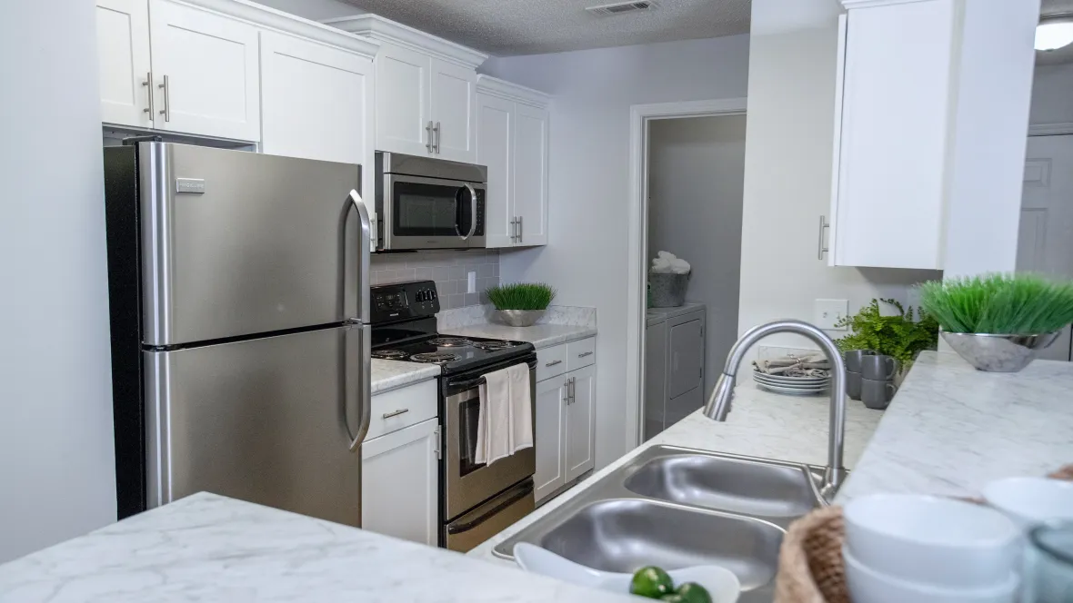 Upgraded kitchen featuring Carrara marble-inspired countertops, stainless-steel appliances, and white shaker cabinetry. The galley-style layout opens to the living room with a breakfast bar, creating an elegant and functional space.