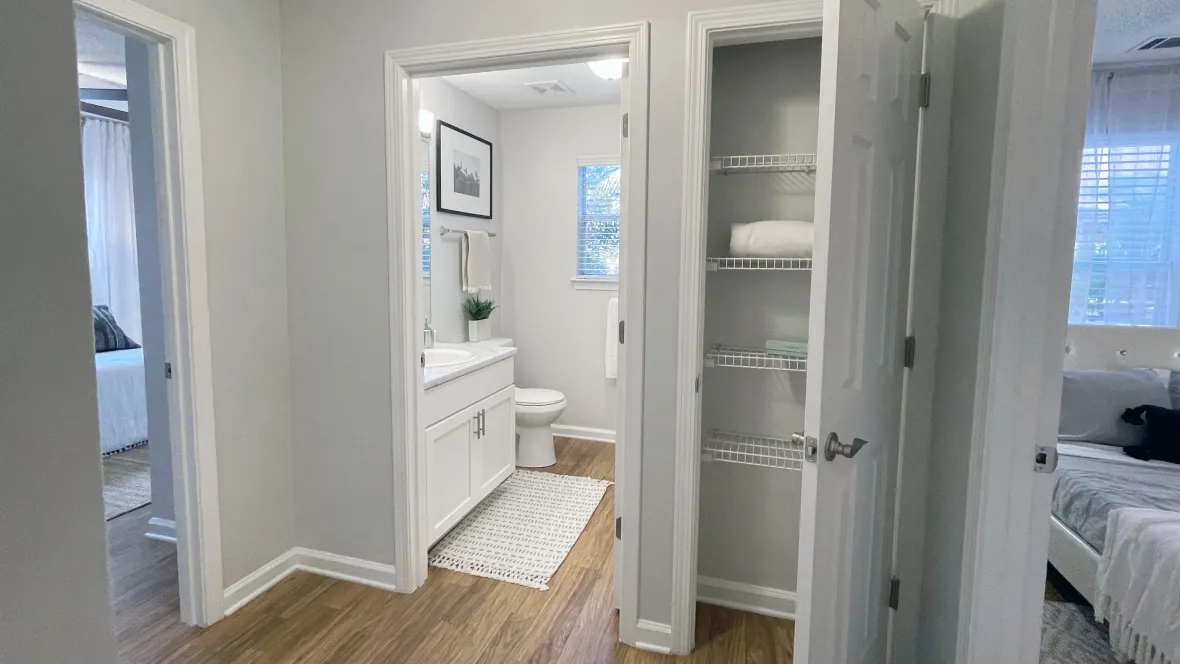 A linen closet in the hallway of an apartment home, next to the bathroom, offering a stylish and organized storage solution for residents.