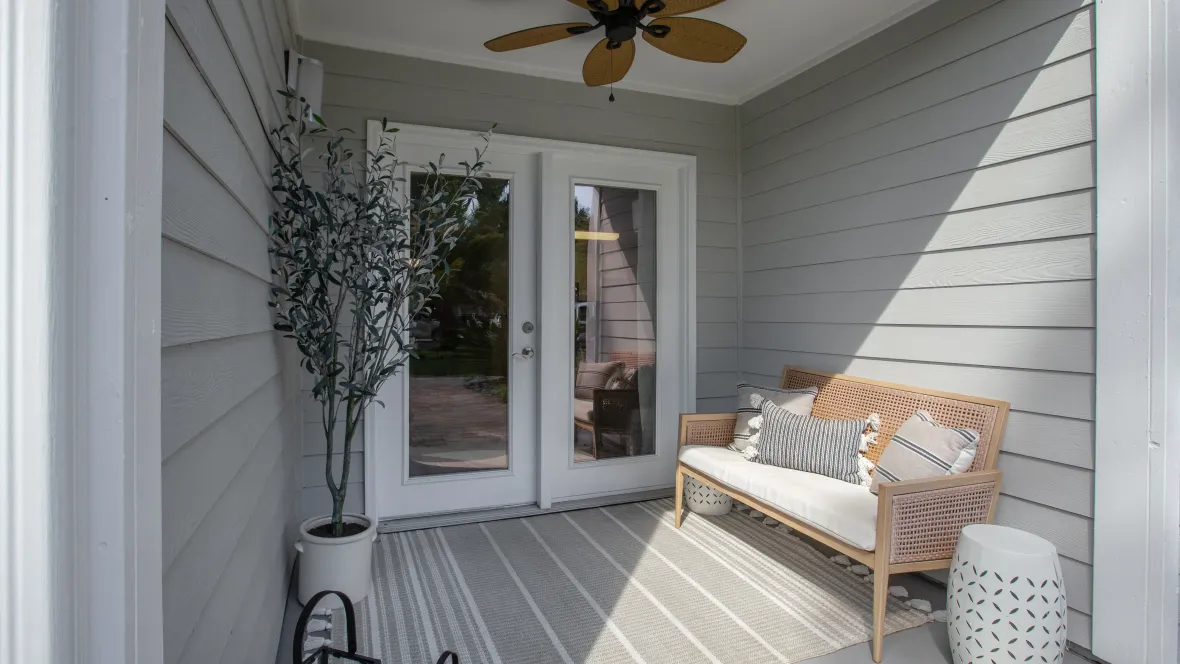 A private patio with outdoor ceiling fan and French doors leading into an apartment home.