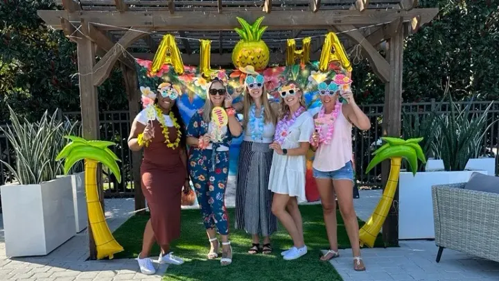 A group of residents pose for a photo during our luau party with palm tree balloons on either side of them and a balloon banner that reads "aloha" behind them.