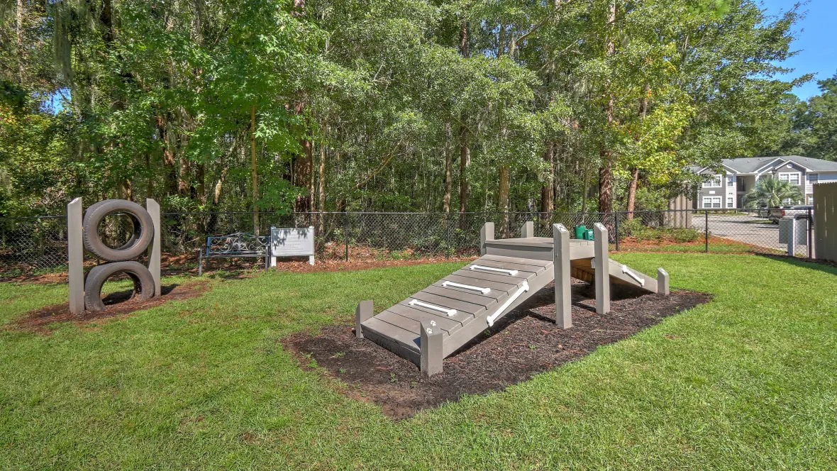 A lush, grassy fenced dog park with agility equipment, including a ramp and tires to wear out your dog.